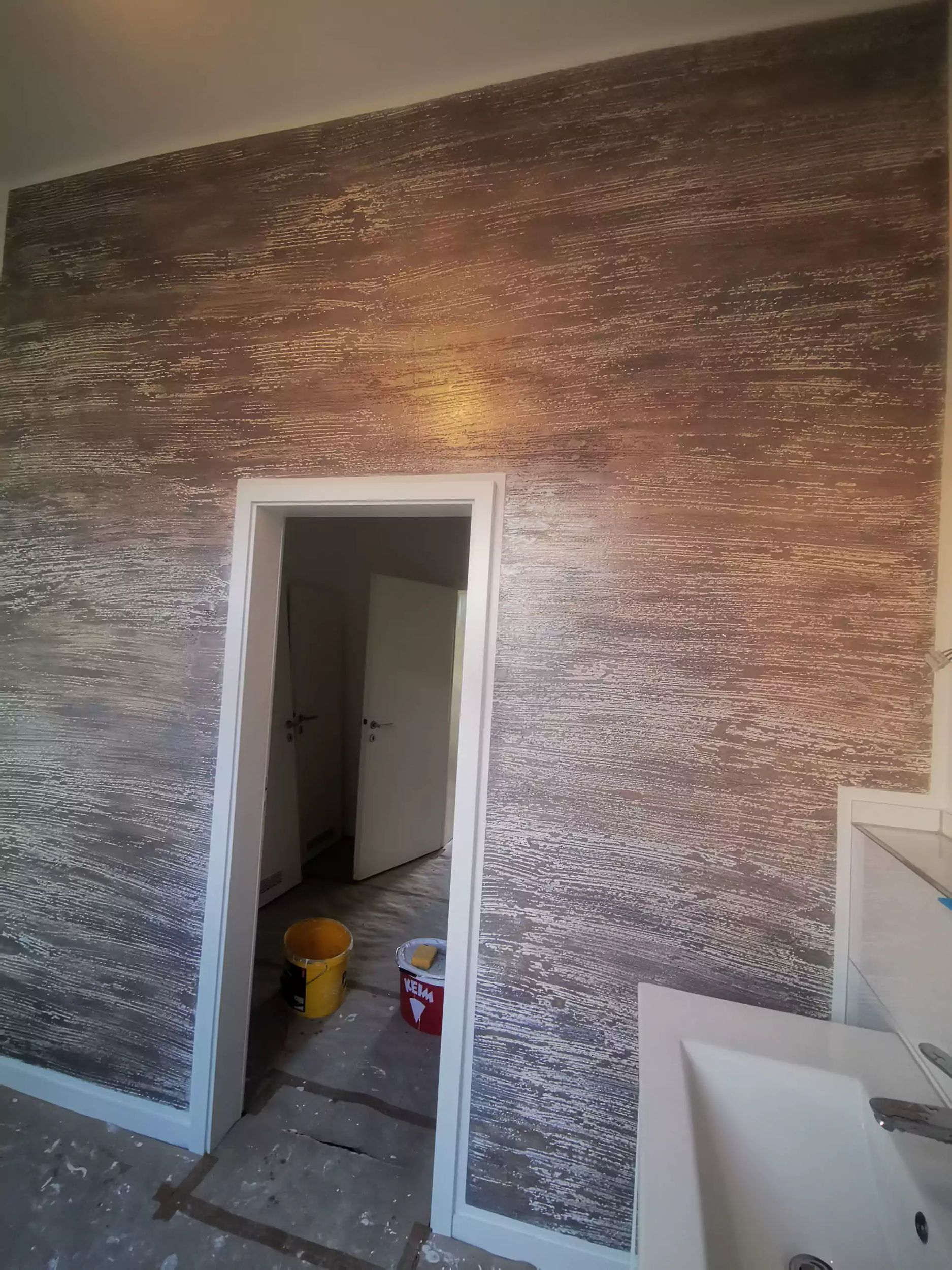 Strukturierte braun-silberne Wand mit offener Tür und weißem Waschbecken.