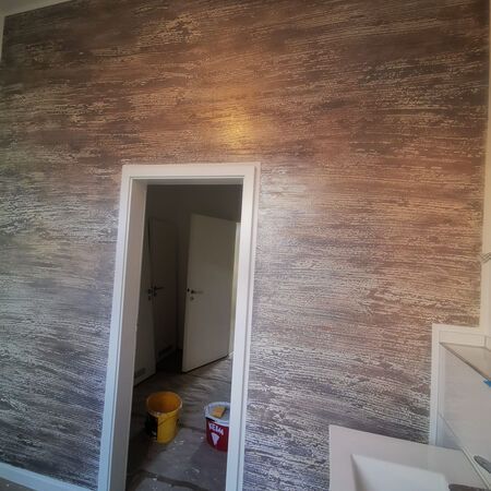 Zimmer mit strukturierter braun-silberner Wand, weißem Türrahmen und teilweise sichtbarem weißem Waschbecken.