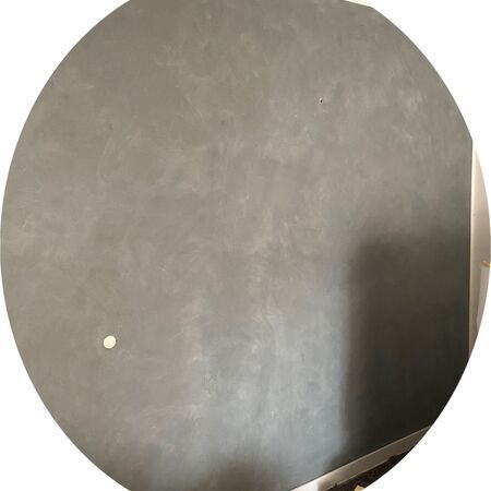 Graue, kreisrunde Wand mit strukturierter Oberfläche und einem einzelnen weißen Punkt.