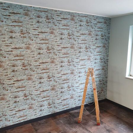 Zimmer mit gemusterter blauer Tapete, braunem Fußboden, kleiner Holzleiter und Fenster.