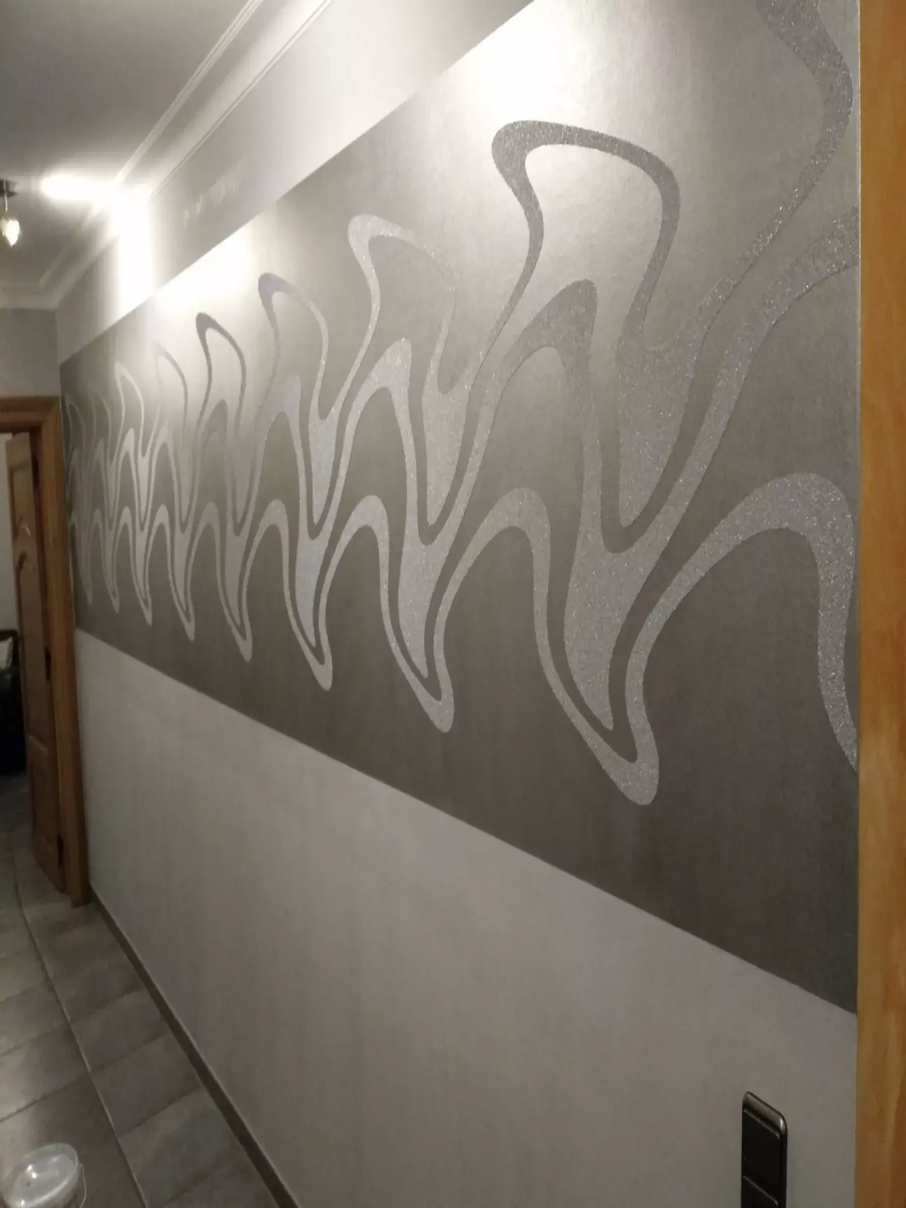 Ein Flur mit einem dekorativen, grau-weißen Wellenmuster im oberen Bereich der Wand.