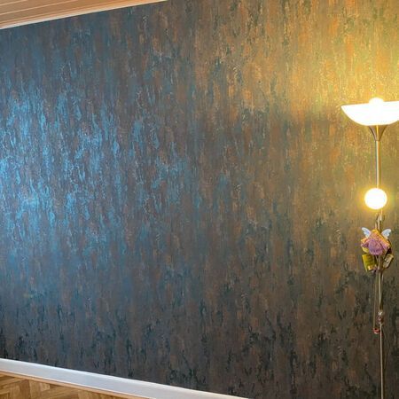 Strukturierte Wand in Türkis- und Bronzetönen, beleuchtet von einer warmen Lampe, mit Holzleisten.