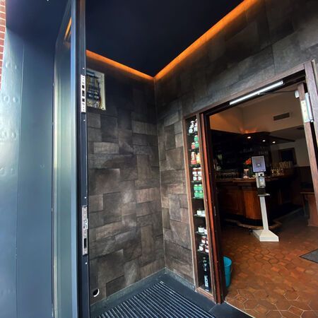 Eingang zu einer Bar mit offenen Türen, dunkler Steinwand, einem Regal mit Getränken.