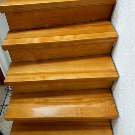 Holztreppe mit heller Lackierung und sichtbarer Holzmaserung vor einer weißen Wand.