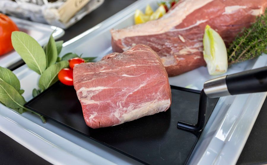 Ein Stück rohes Fleisch liegt auf einem weißen Teller auf einem Tisch.