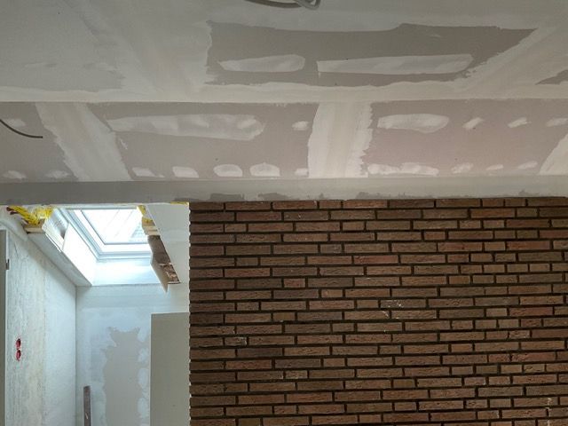 Teilweise fertiggestellter Innenraum mit Ziegelwand, weißer Gipskartondecke und Dachfensteröffnung