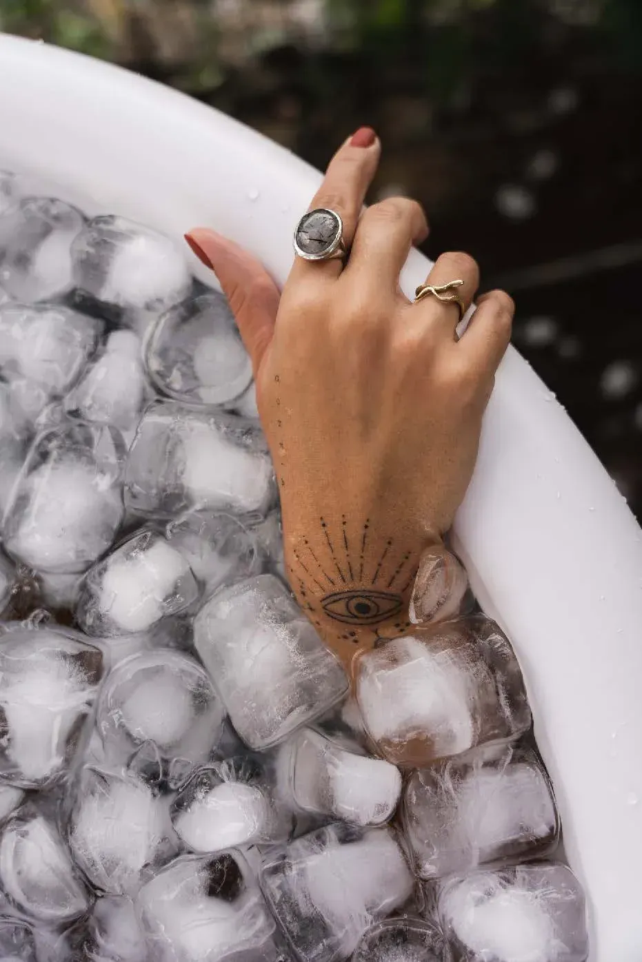 La mano de una mujer sobresale de una bañera llena de cubitos de hielo.