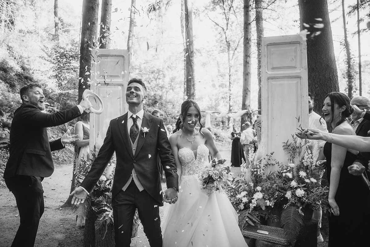 Una fotografía en blanco y negro de unos novios caminando por un bosque.