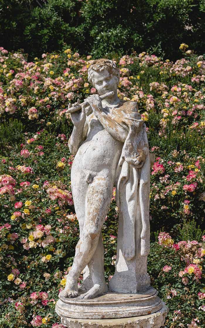 Una estatua de un hombre tocando una flauta frente a un campo de flores.