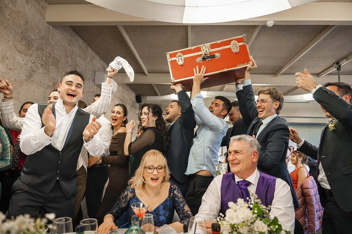 Un grupo de personas está sentada en una mesa en una recepción de boda sosteniendo una maleta.