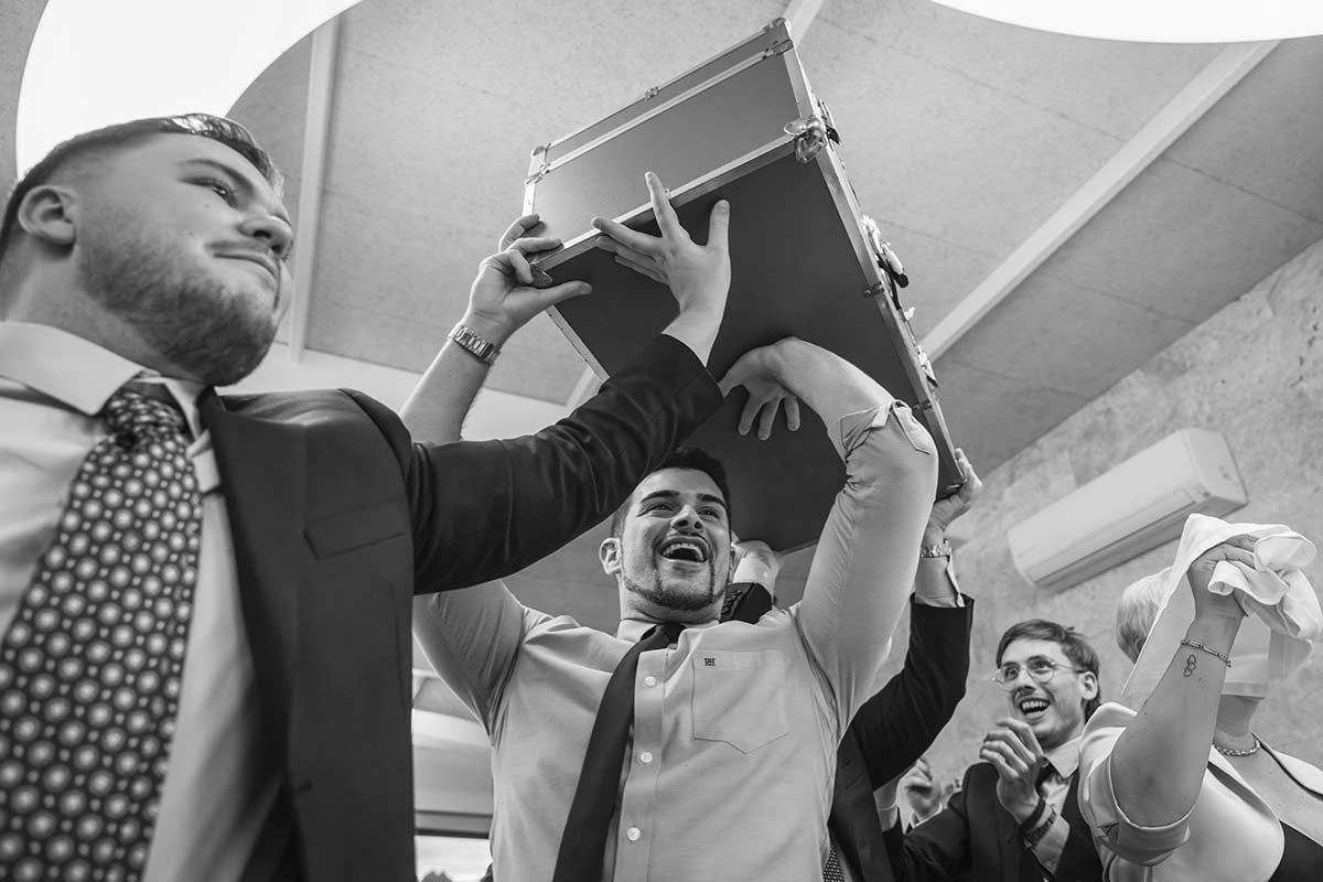 Un grupo de hombres sostiene una maleta sobre sus cabezas.