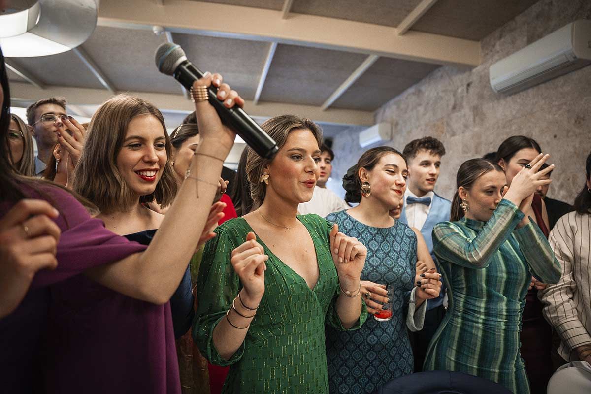 Una mujer con un vestido verde está cantando en un micrófono en una fiesta.