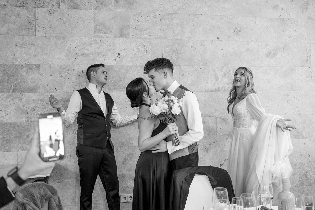 Una fotografía en blanco y negro de una novia y un novio besándose en una recepción de boda.