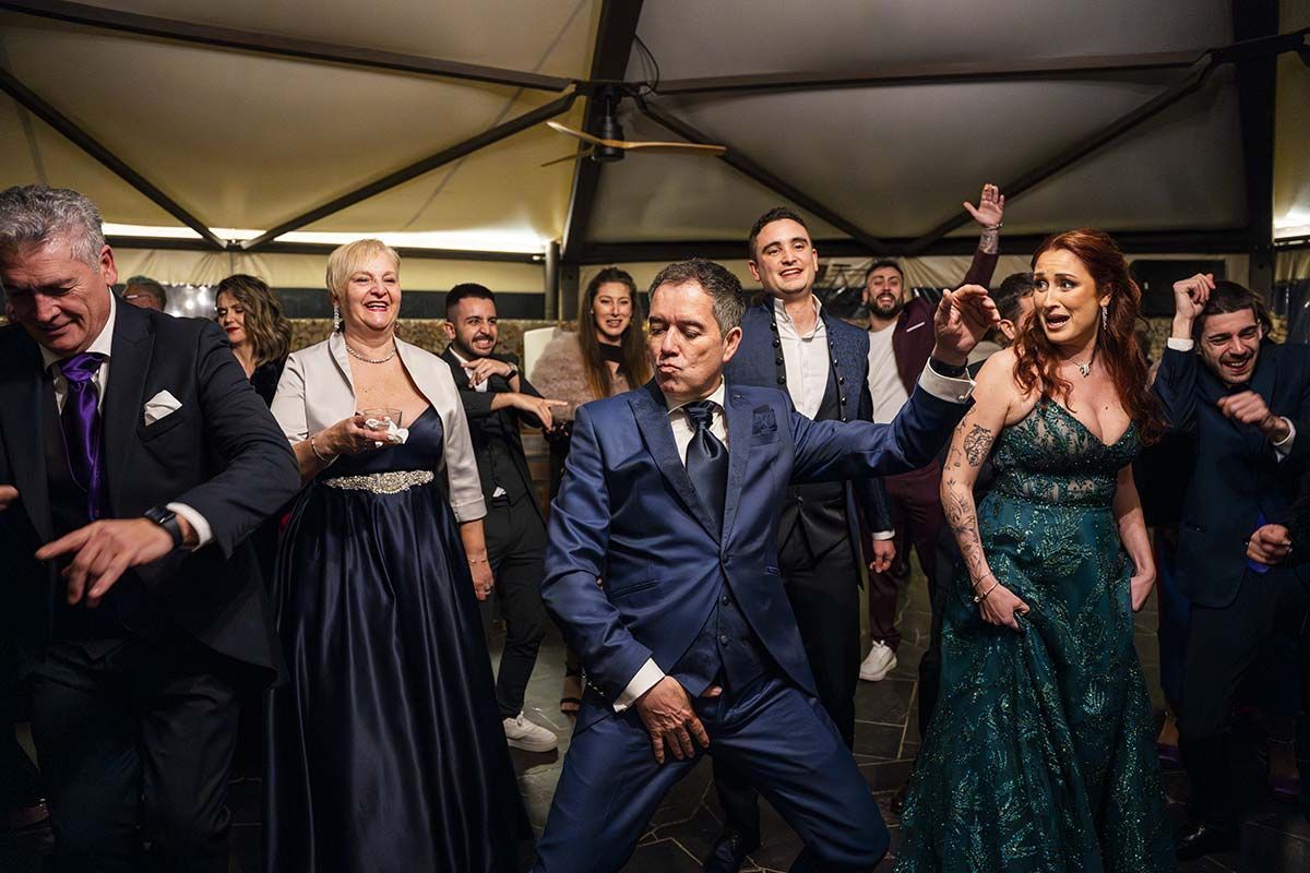 Un hombre con traje está bailando con un grupo de personas en una recepción de boda.