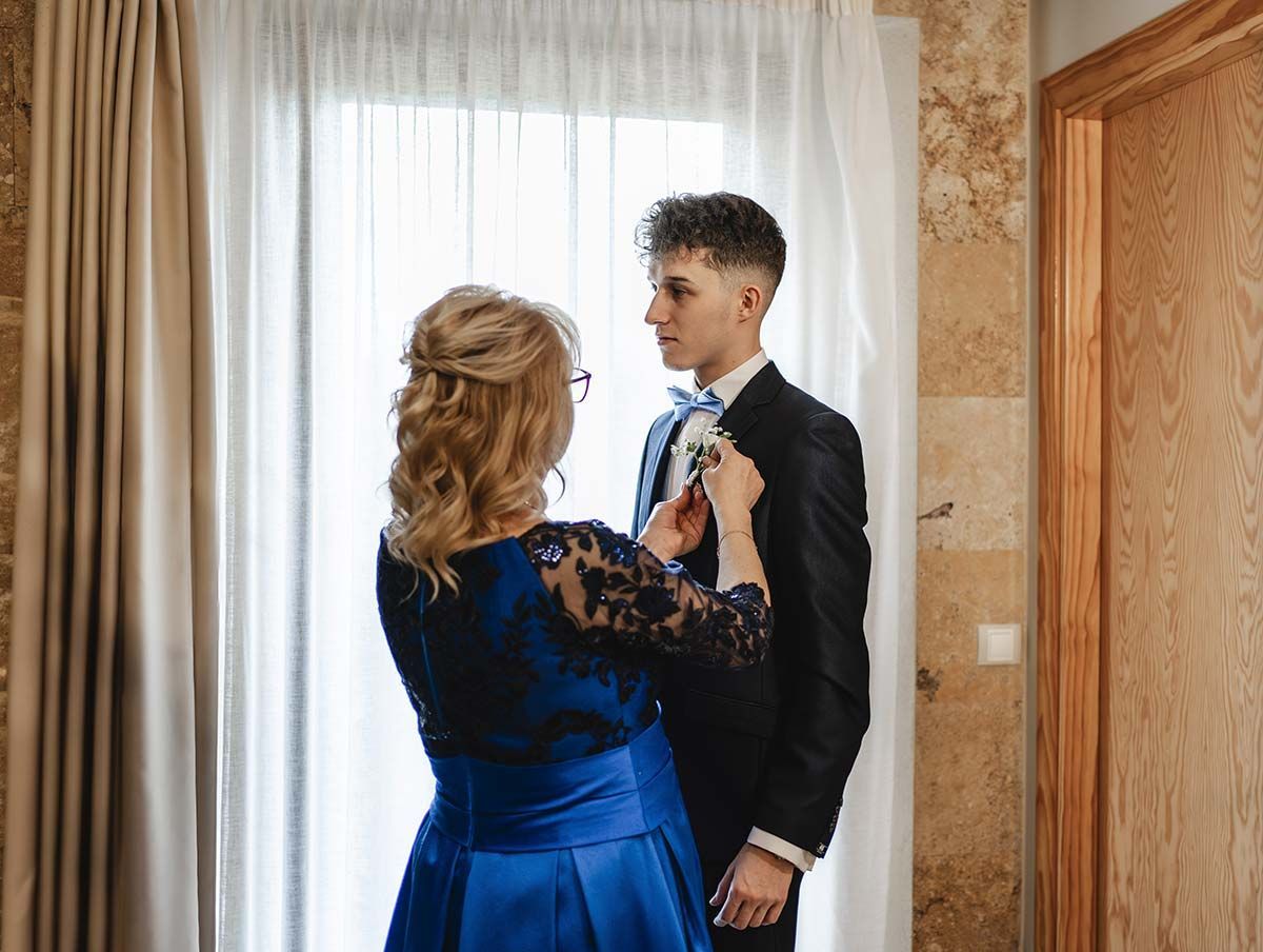 Una mujer con un vestido azul está ayudando a un hombre con traje a atar la corbata.