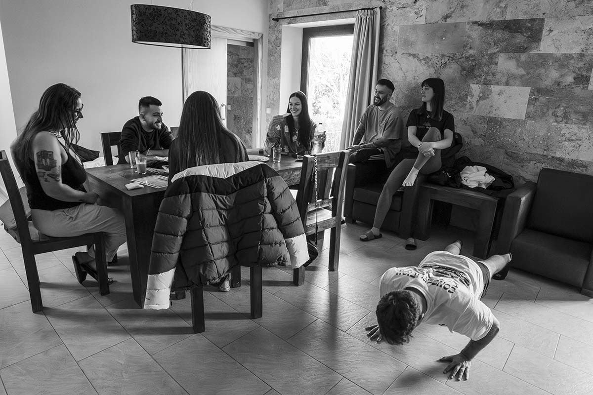 Un grupo de personas está sentado alrededor de una mesa y un hombre está haciendo el pino.