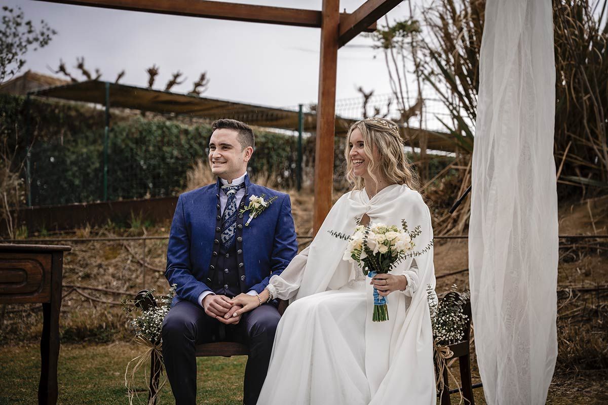 Una novia y un novio están sentados en un banco tomados de la mano.