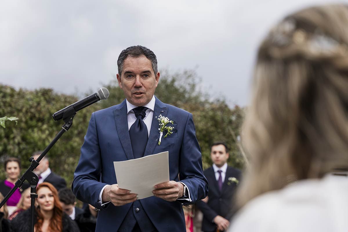 Un hombre con traje y corbata sostiene un trozo de papel delante de un micrófono.