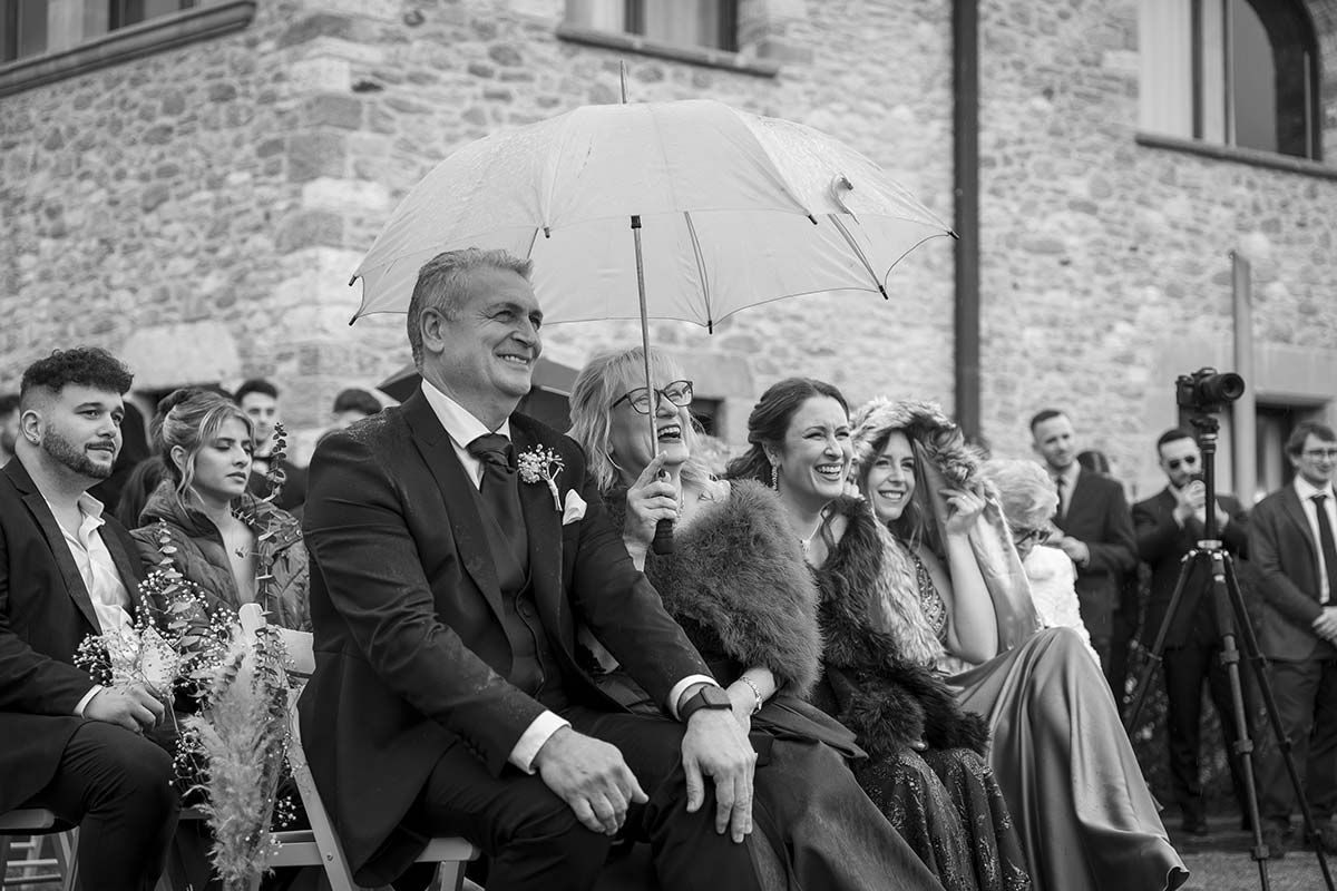 Una fotografía en blanco y negro de un grupo de personas sentadas bajo una sombrilla en una boda.