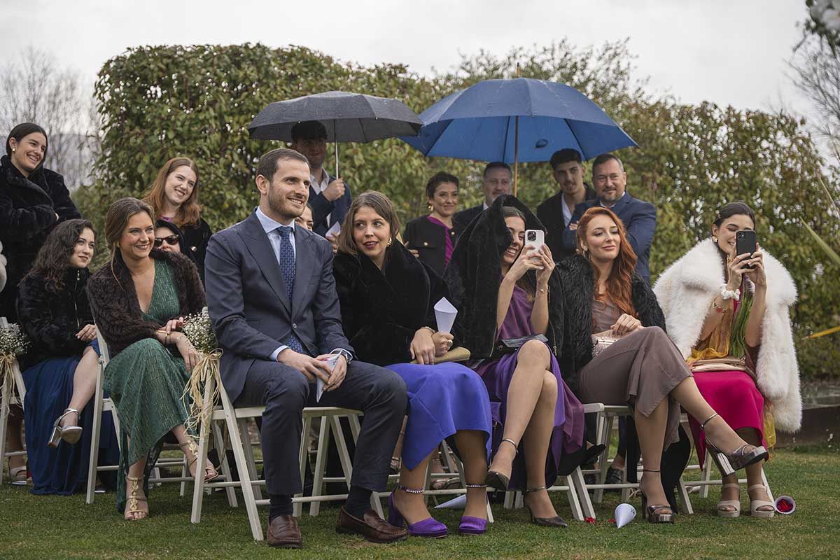 Un grupo de personas están sentadas en taburetes en el césped sosteniendo paraguas.