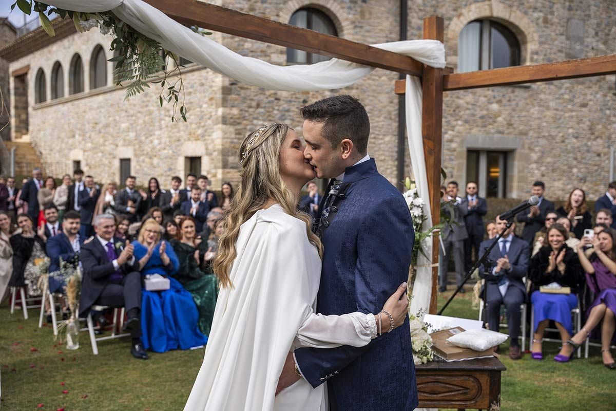 Una novia y un novio besándose delante de sus invitados a la boda.