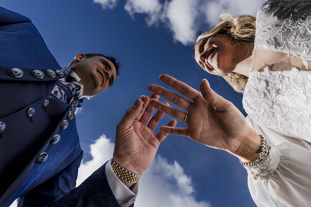 Una novia y un novio se toman de la mano frente a un cielo azul.