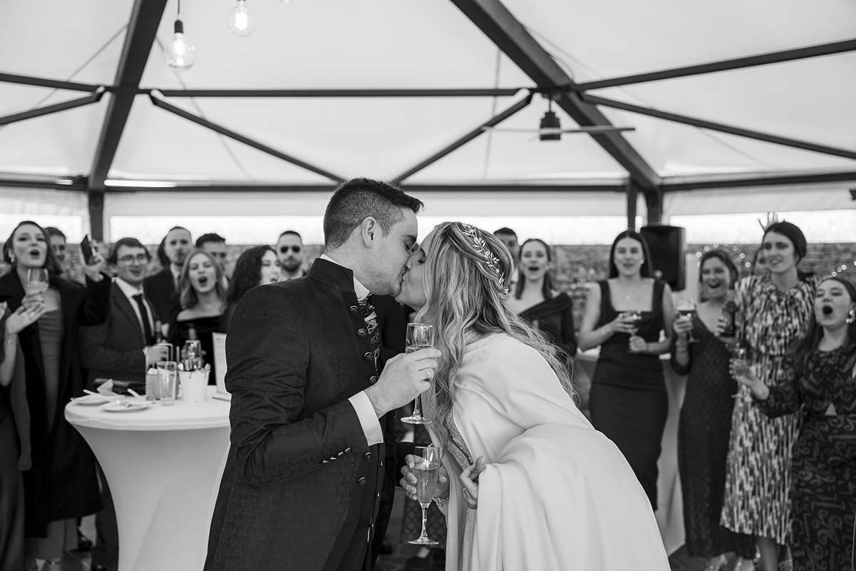 Una novia y un novio se besan delante de sus invitados a la boda.