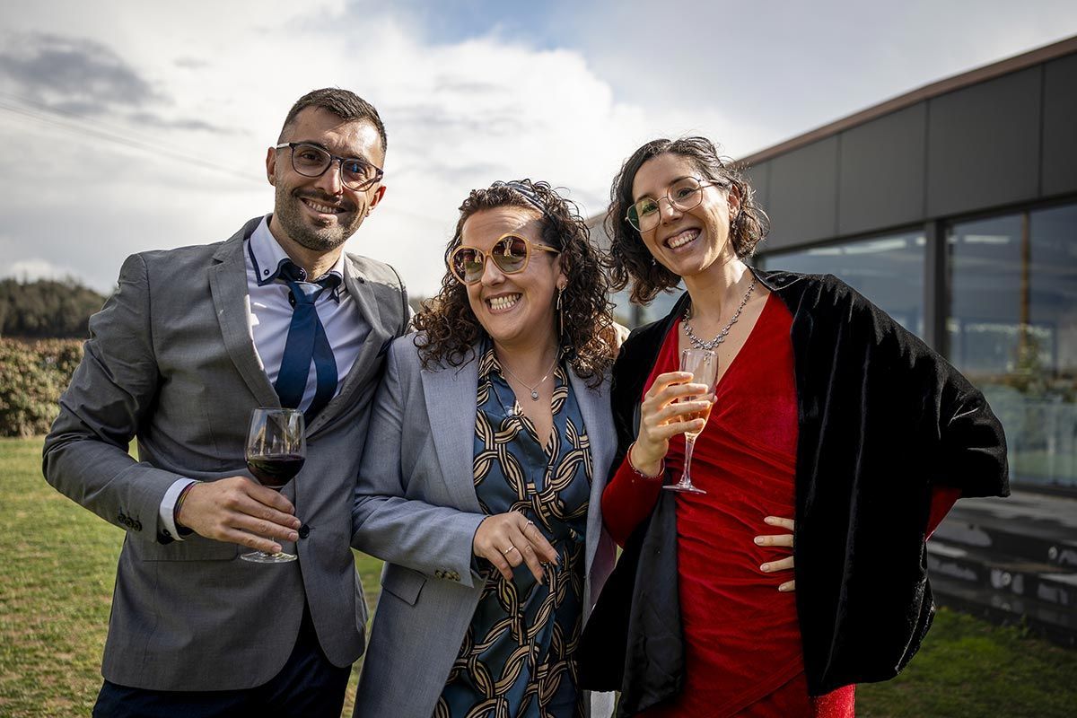 Un hombre y dos mujeres posan para una fotografía mientras sostienen copas de vino.