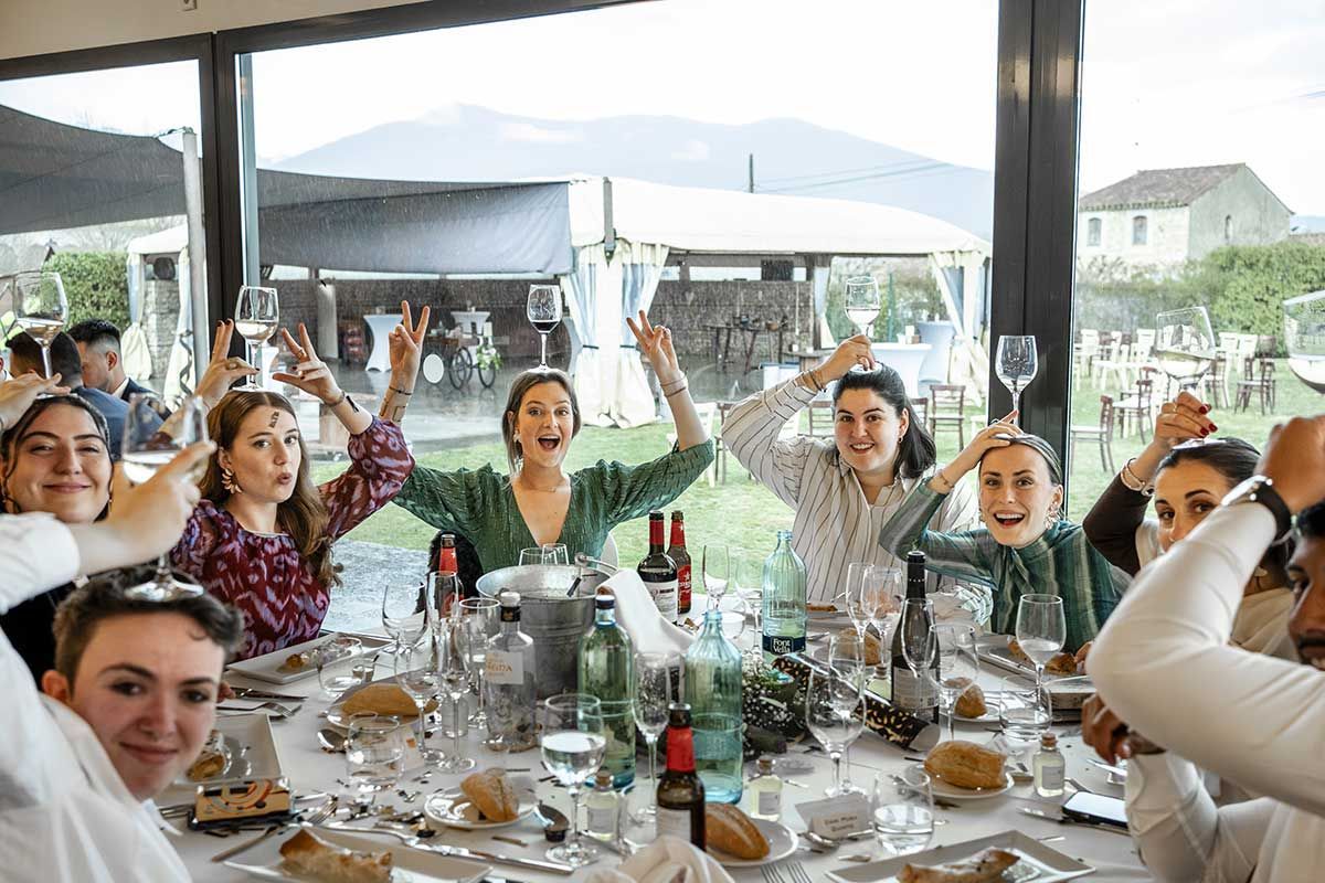 Un grupo de personas está sentada en una mesa con los brazos en el aire.