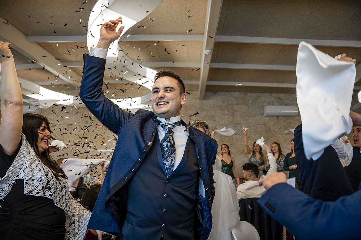 Un hombre con traje y corbata está lanzando confeti al aire en la recepción de una boda.