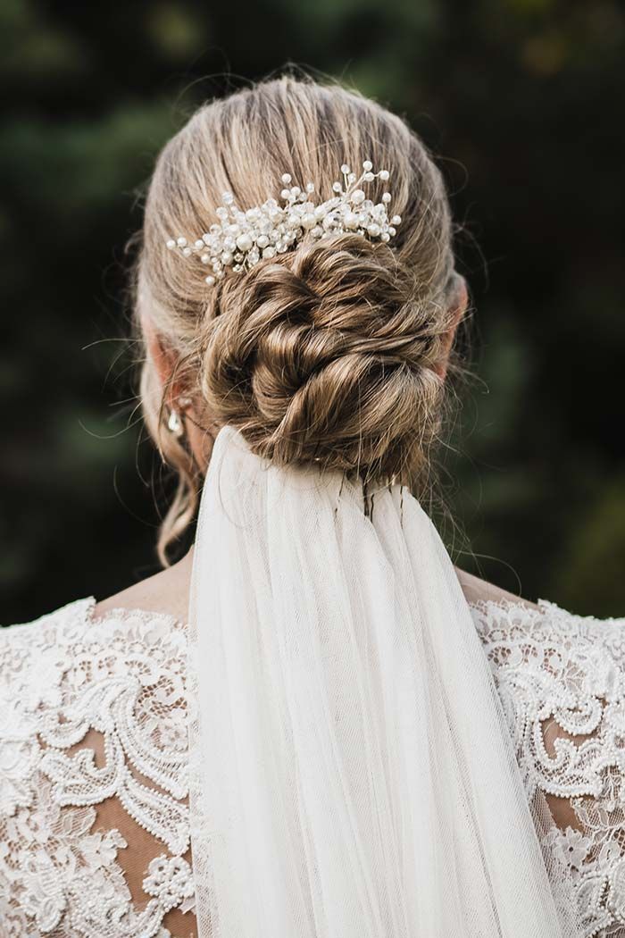 La espalda de una novia con velo y un moño trenzado.