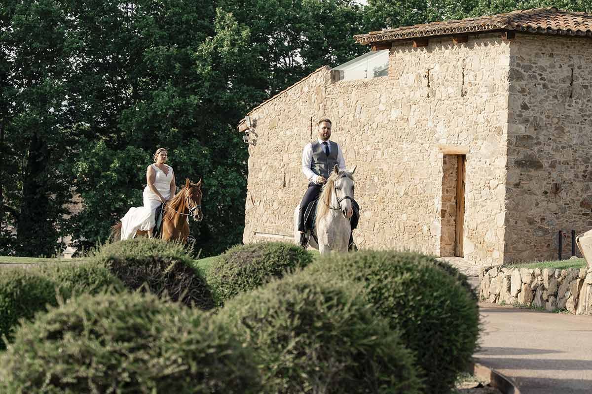 Una novia y un novio montan a caballo frente a un edificio de piedra.