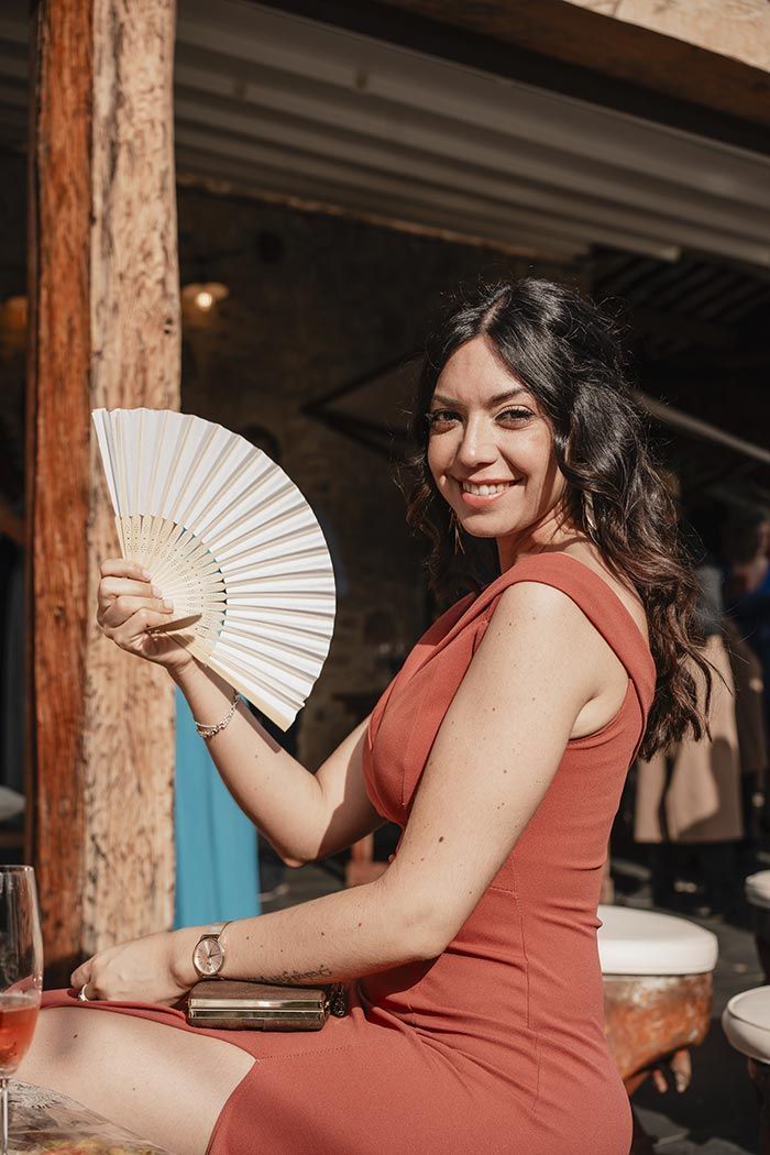 Una mujer con un vestido rojo sostiene un abanico blanco mientras está sentada en una mesa.
