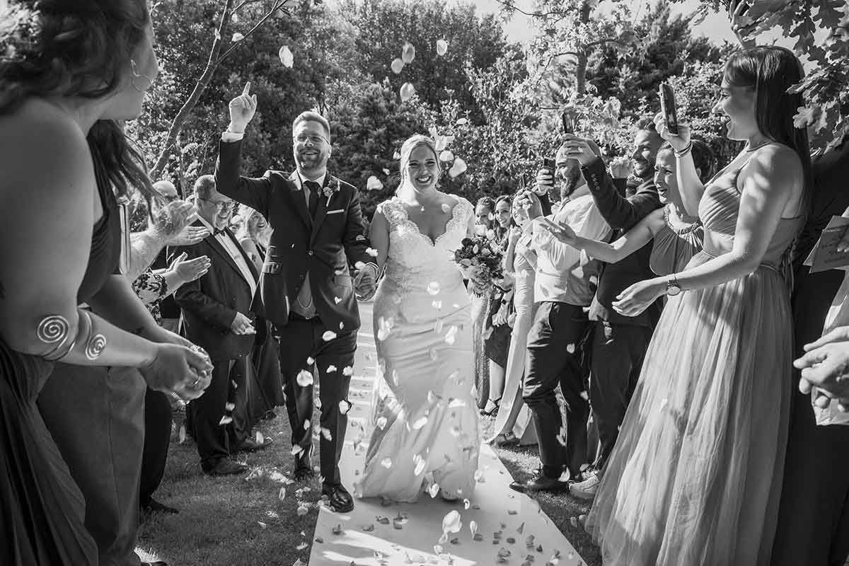Una fotografía en blanco y negro de una novia y un novio siendo bañados con confeti en su boda.