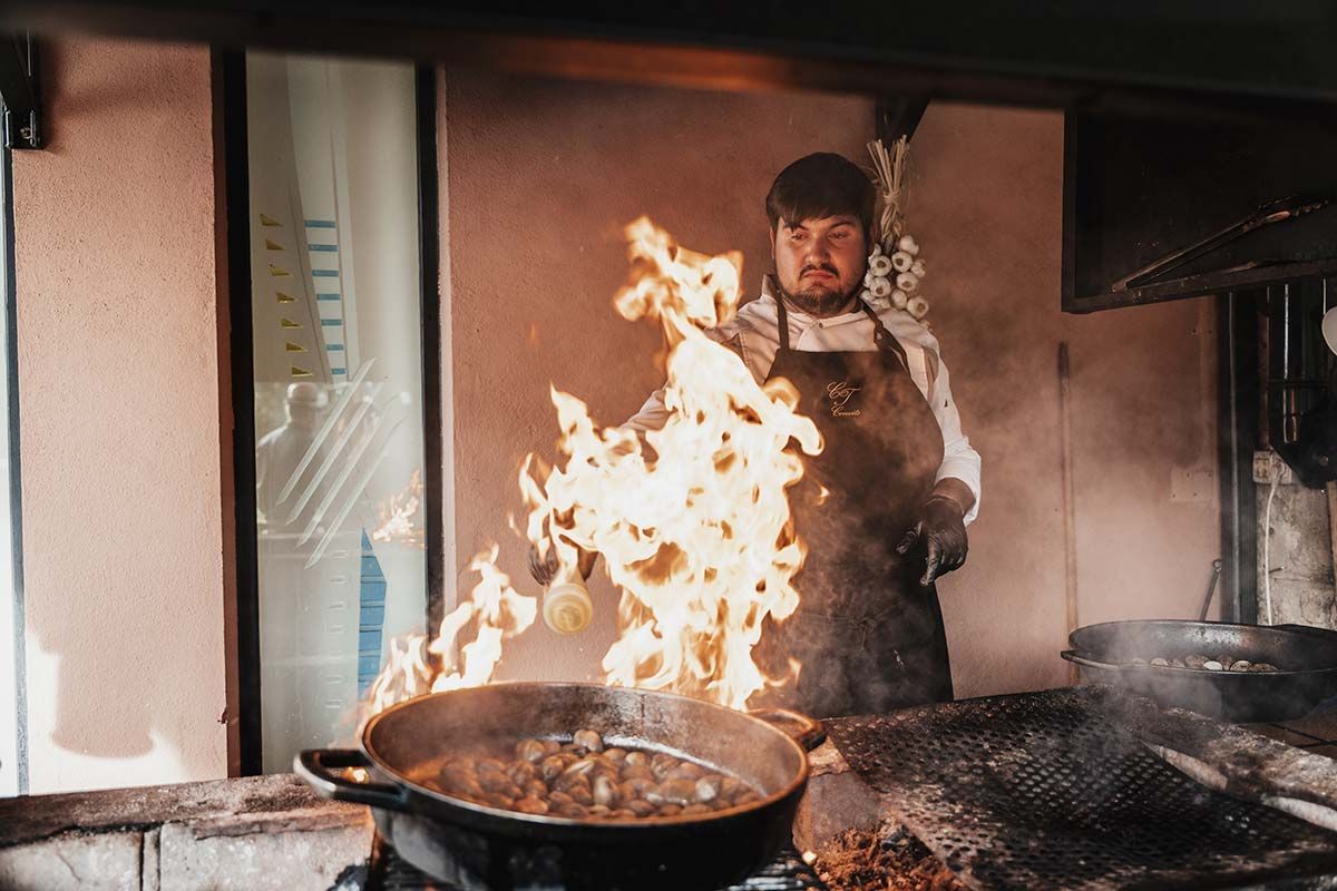 Un hombre está cocinando comida en una sartén sobre una estufa de la que salen llamas.