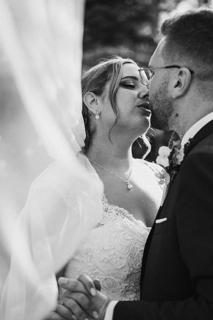 Una novia y un novio se besan bajo un velo en una foto en blanco y negro.