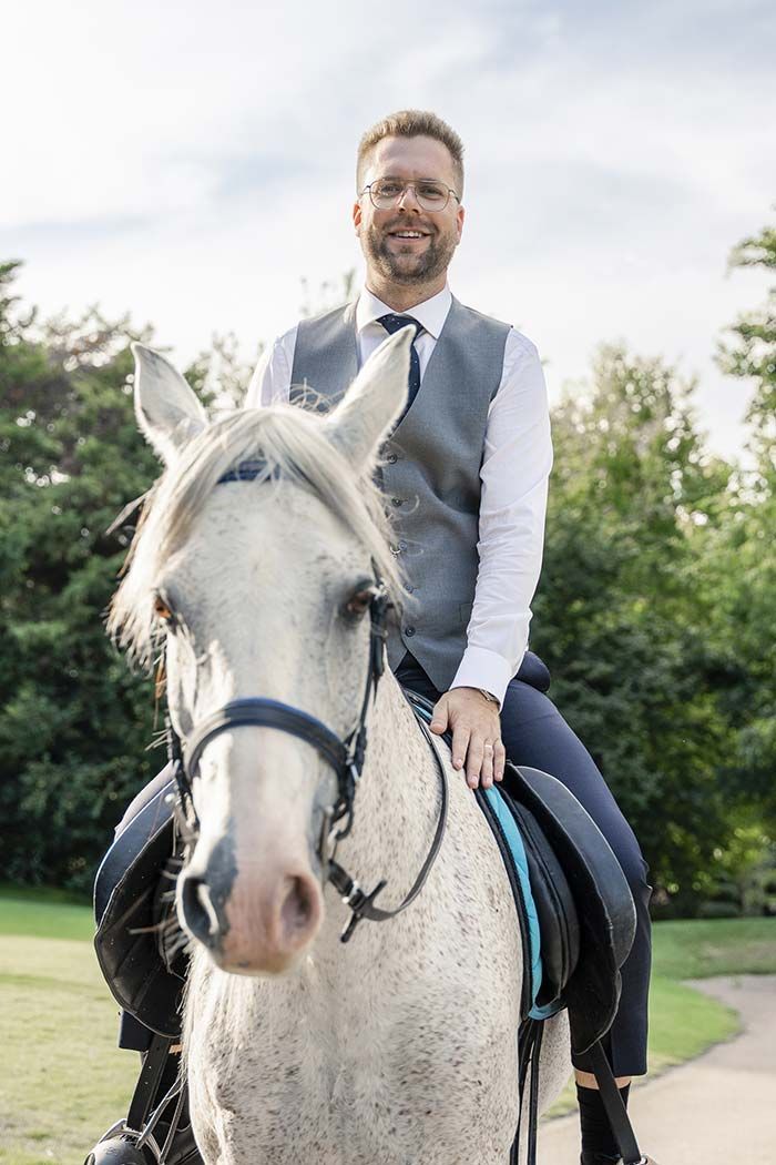 Un hombre con traje monta un caballo blanco.