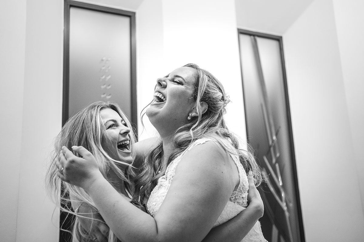 Dos mujeres se abrazan y se ríen frente a un espejo.