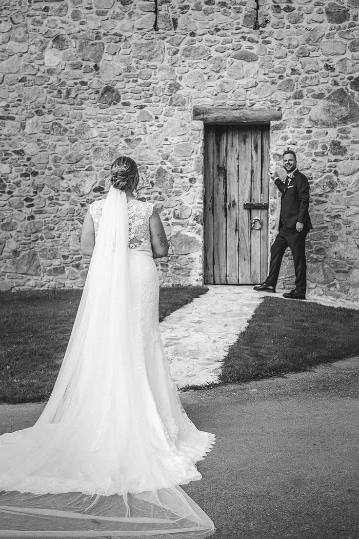 Una fotografía en blanco y negro de una novia y un novio de pie frente a un muro de piedra.