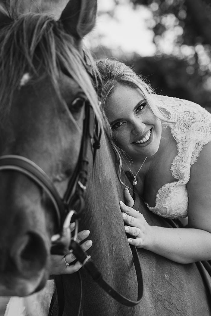 Una fotografía en blanco y negro de una novia abrazando a un caballo.