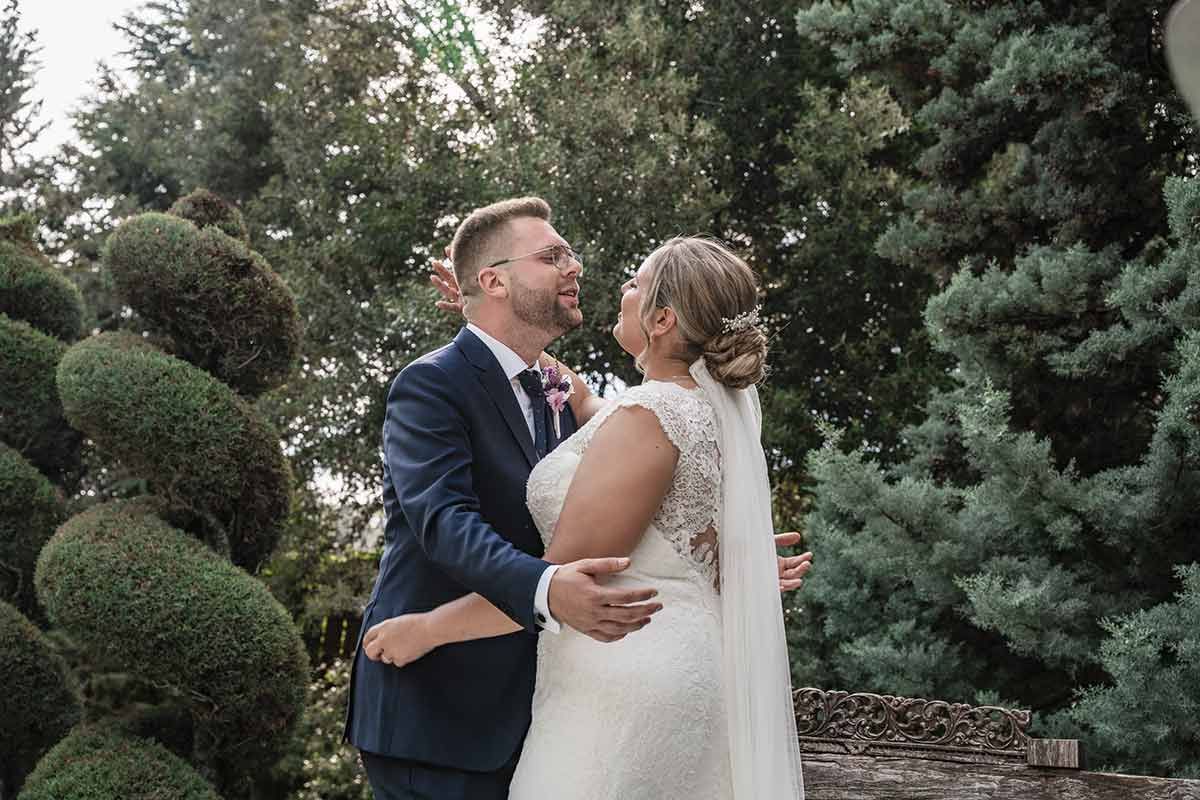 Una novia y un novio posan para una foto delante de unos árboles.