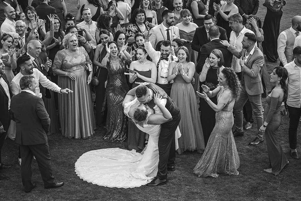 Una fotografía en blanco y negro de una novia y un novio besándose delante de sus invitados a la boda.
