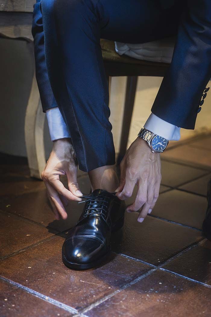 Un hombre con traje se ata los zapatos en un suelo de baldosas.