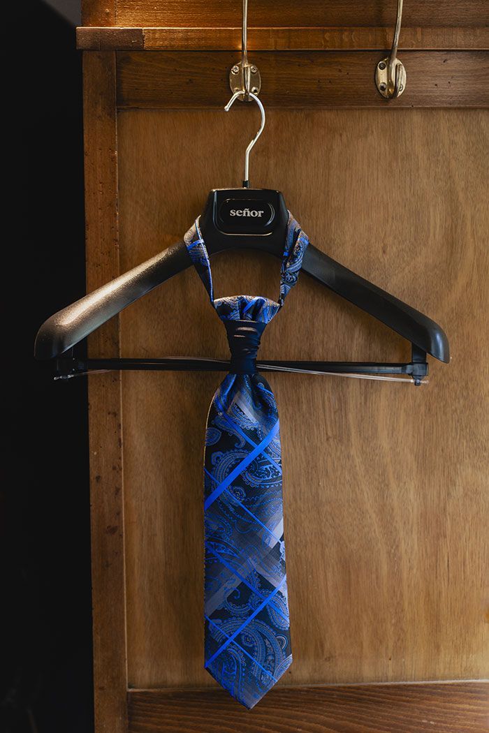 Una corbata azul cuelga de una percha negra en una pared de madera.