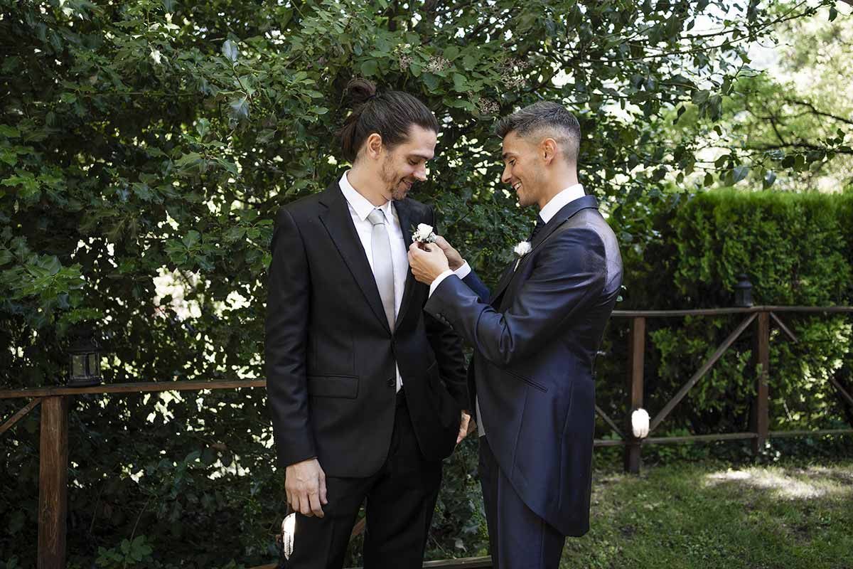 Dos hombres de traje están parados uno al lado del otro frente a unos árboles.