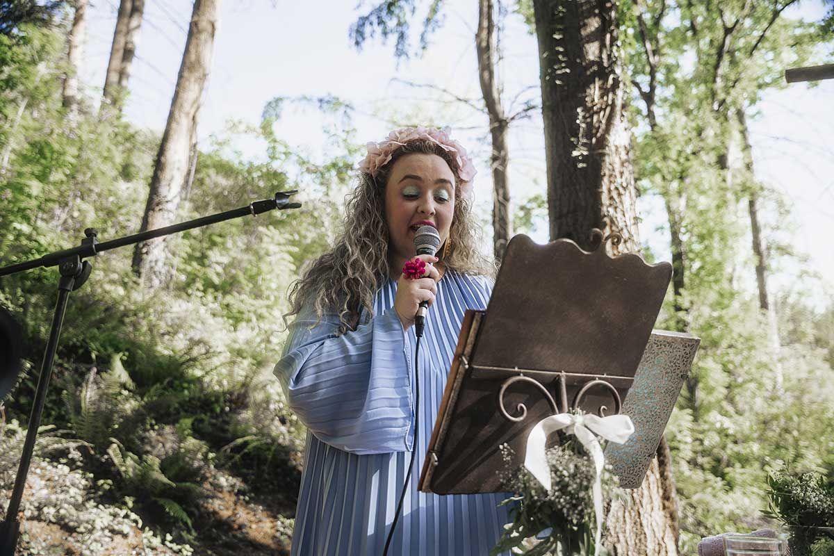 Una mujer está cantando con un micrófono en el bosque.