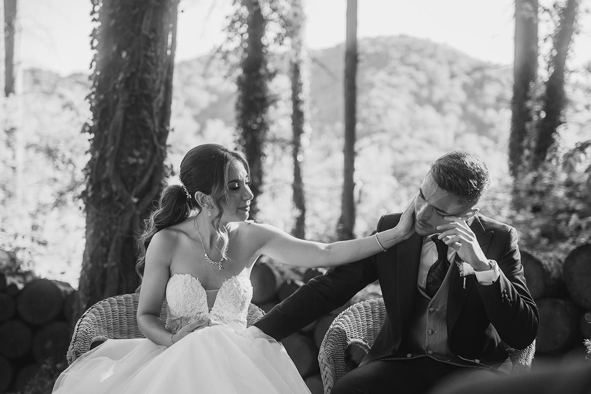 Una fotografía en blanco y negro de una novia y un novio sentados en sillas en el bosque.