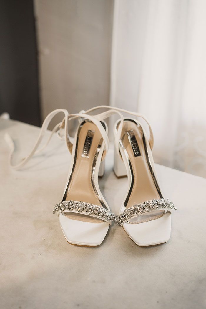 Un par de zapatos de boda blancos están sentados sobre una cama.