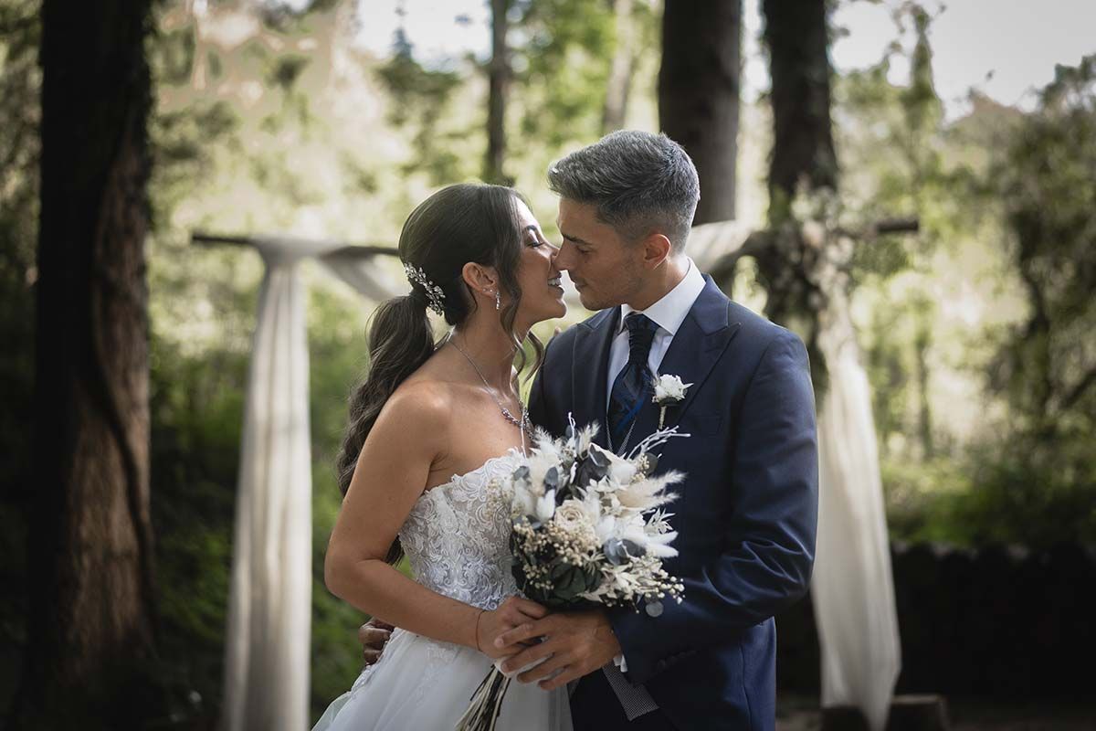 Una novia y un novio se besan en el bosque.