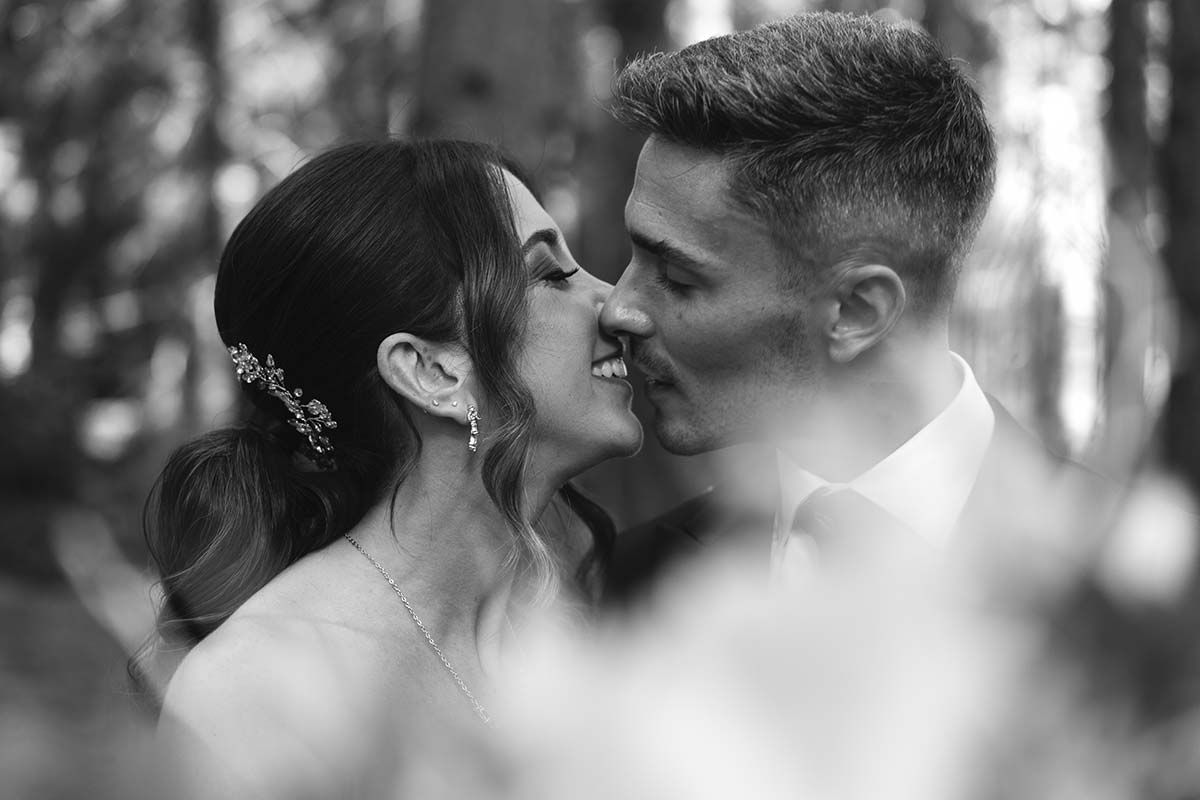 Una novia y un novio se besan en el bosque en una foto en blanco y negro.